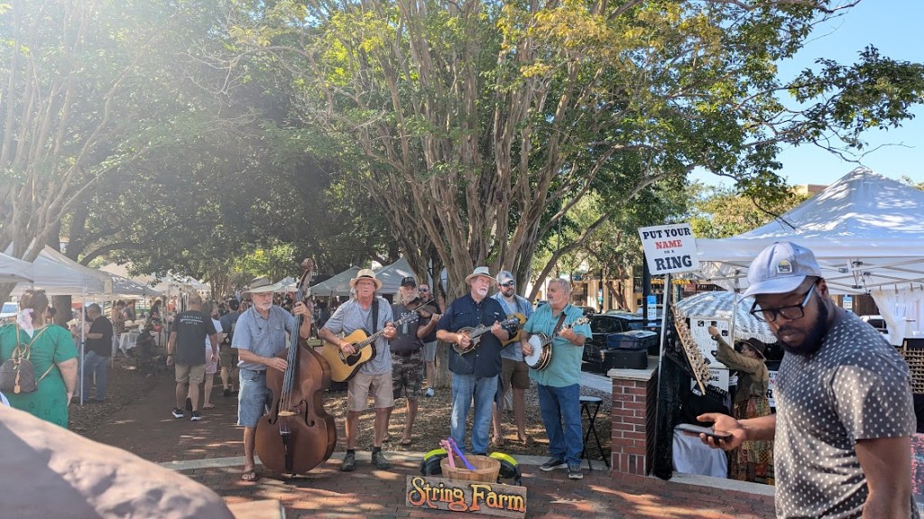 Street scene with trees and a crowd: a bluegrass band is in center
