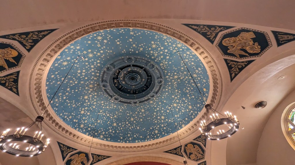 Interior of a church, spotlighting a blue dome decorated with golden stars 