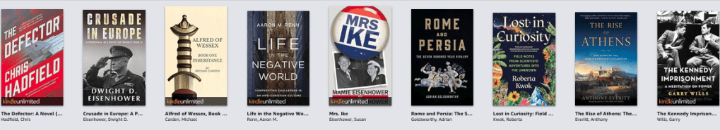 A row of books from a Kindle shelf, depicting The Defector, Crusade in Europe, Alfred of Wessex, Life in the Negati e World, Mrs Ike, Rome and Persia, Lost in Curiosity, The Rise of Athens, and The Kennedy Imprisonment
