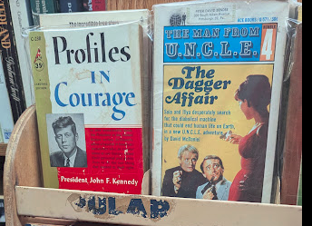 A rare books shelf showing a first-edition Profiles in Courage and a novel from The Man from UNCLE Series