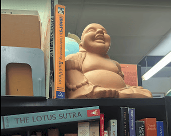 A statue of a laughing Buddha amid books on Buddhism